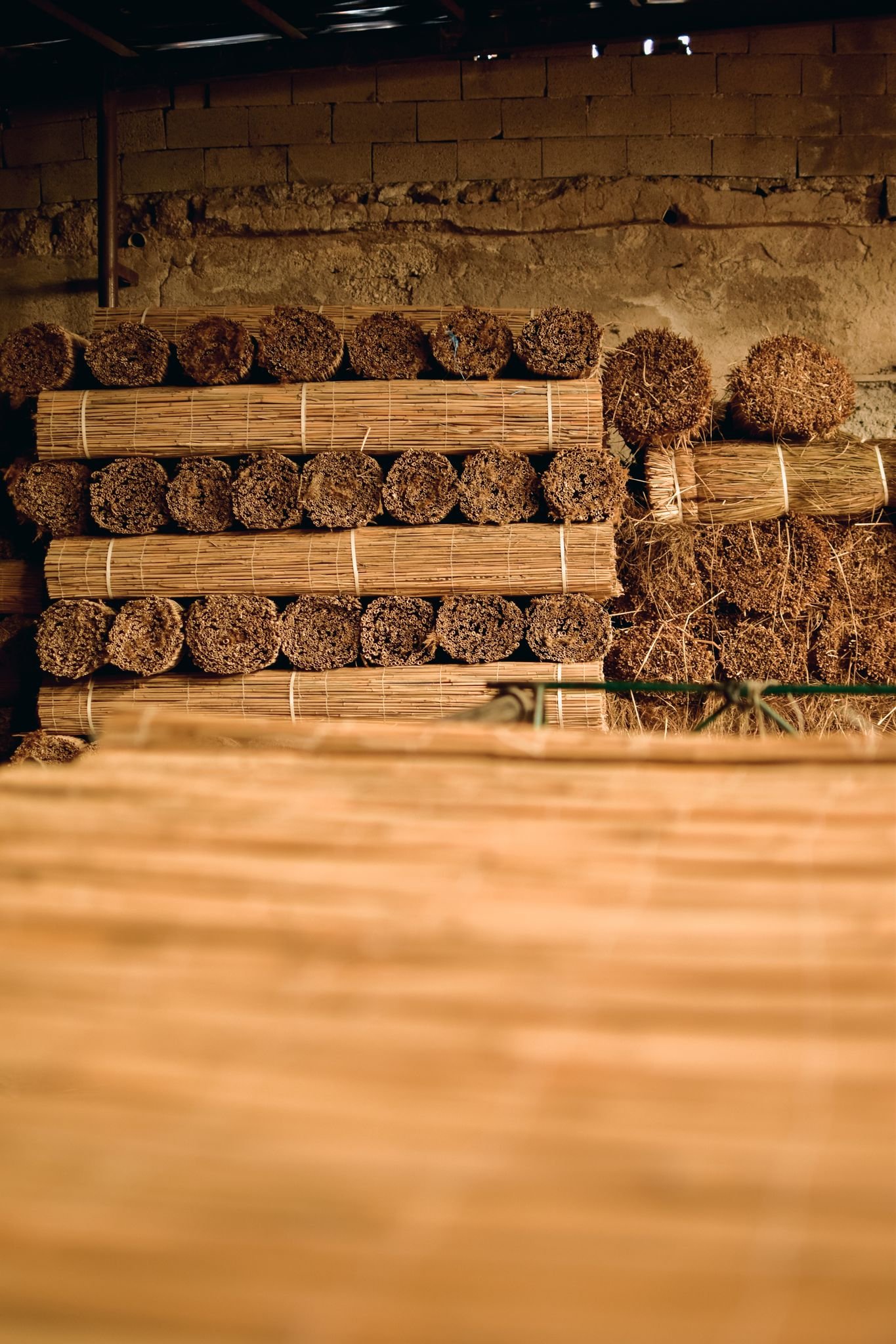 Rows of handmade straw mats arranged in a rustic cellar, showcasing natural texture and craftsmanship.
